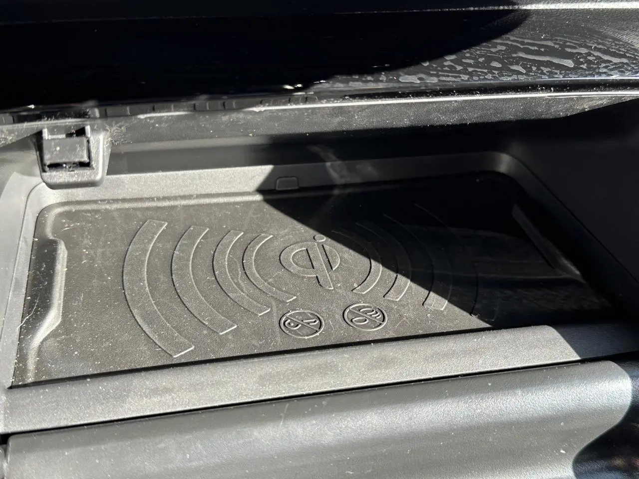 Gros plan sur le tapis de recharge sans fil Qi noir dans la console centrale de la Peugeot 208 Hybrid 145 e-DSC6 GT 2024.