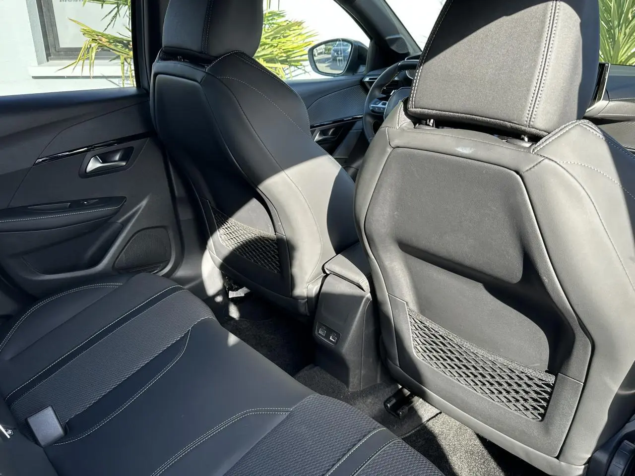 Vue arrière intérieure montrant les sièges noirs et les ports USB à l'arrière des sièges avant du Peugeot 208 Hybrid 145 GT.