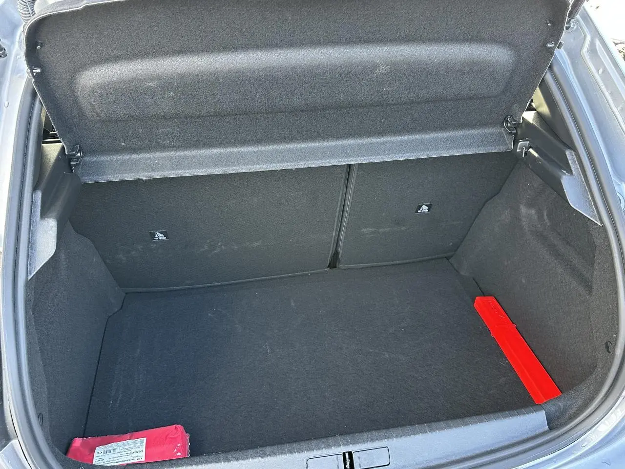 Coffre ouvert d'une Peugeot 208 Hybrid 145 gris Artense, montrant un espace de rangement vide avec un triangle de signalisation rouge.