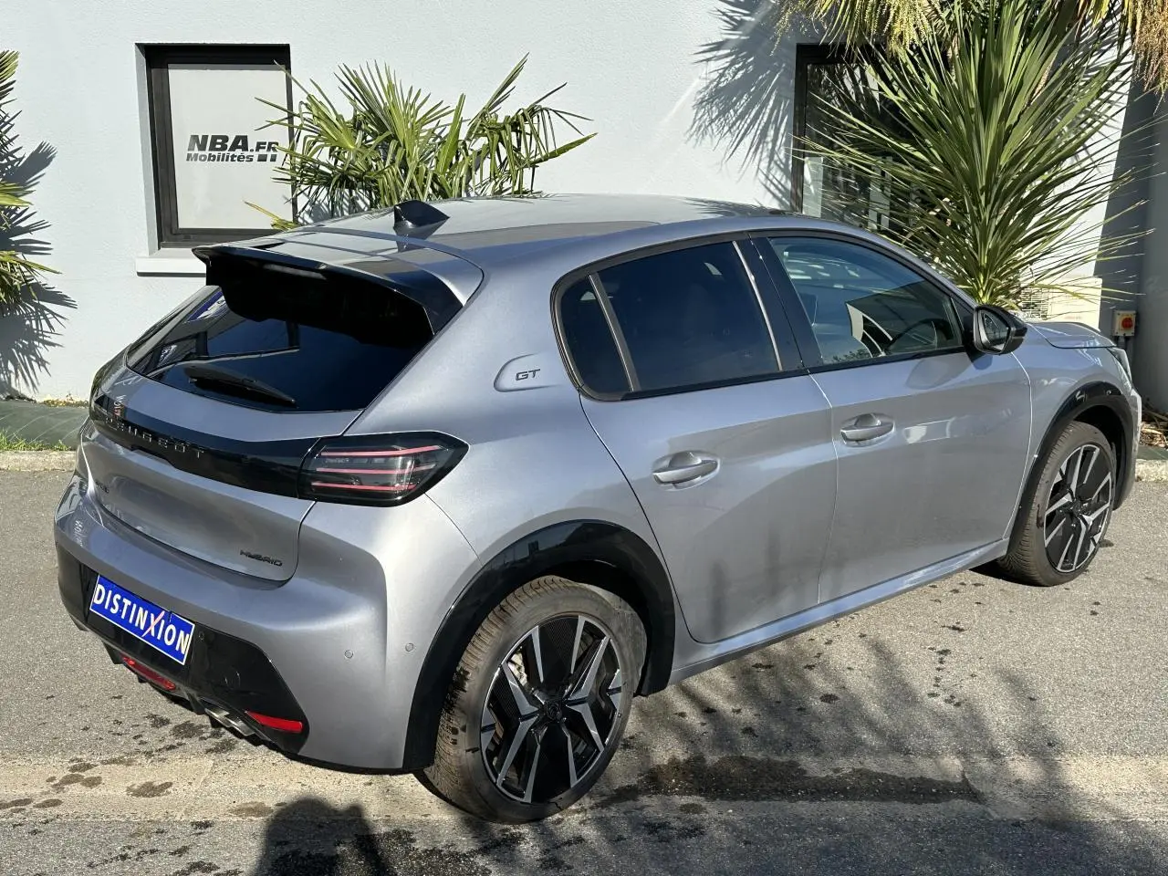 Vue 3/4 arrière droite d'une Peugeot 208 Hybrid 145 GT gris Artense avec jantes alliage bi-tons et badge GT sur l'aile arrière