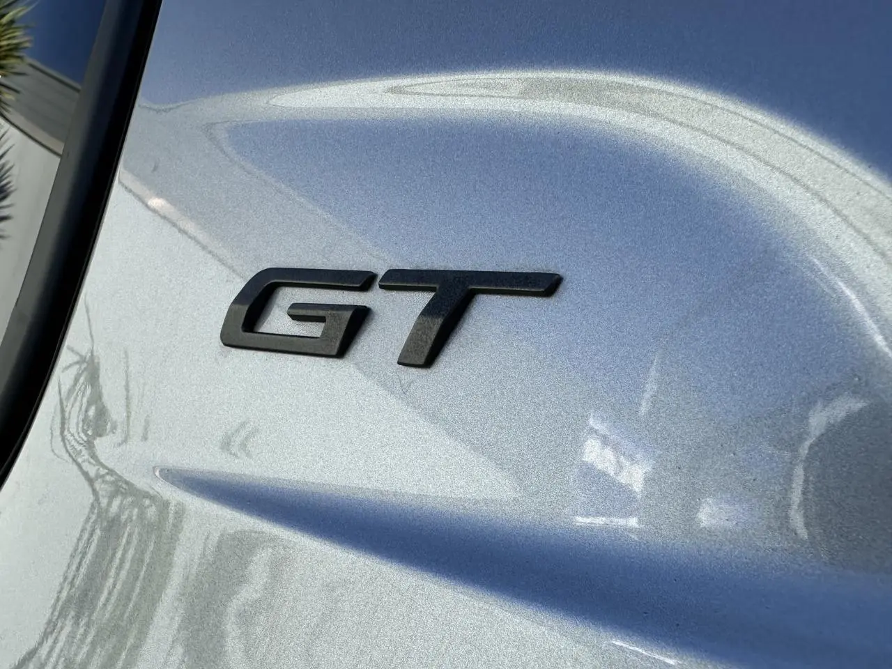 Gros plan sur l’inscription GT noire sur la carrosserie gris Artense d’une Peugeot 208 Hybrid 145 e-DSC6 GT.