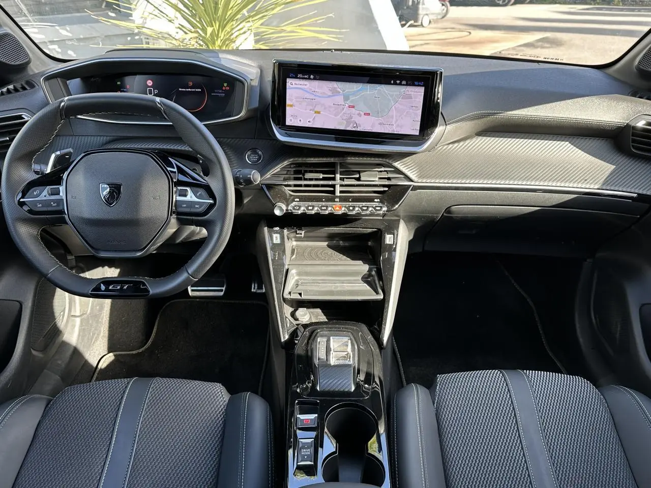 Intérieur Peugeot 208 Hybrid 145 GT vu de face, tableau de bord noir avec écran tactile GPS 10 pouces et volant compact cuir.