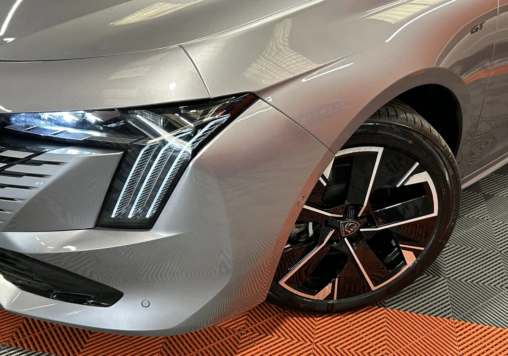 Gros plan sur l'avant droit gris artense du Peugeot 508 SW GT 2024, mettant en valeur le phare LED et la jante noire et argentée.