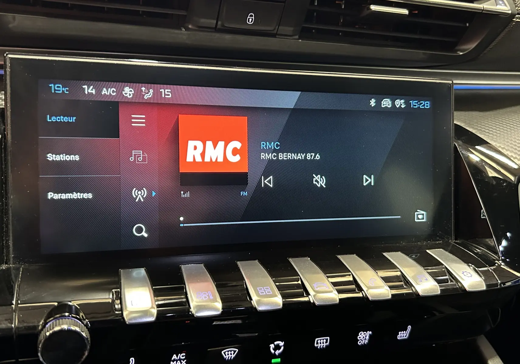 Écran tactile central de la Peugeot 508 SW 2024 affichant la radio RMC, avec commandes climatisation et boutons métalliques en dessous.