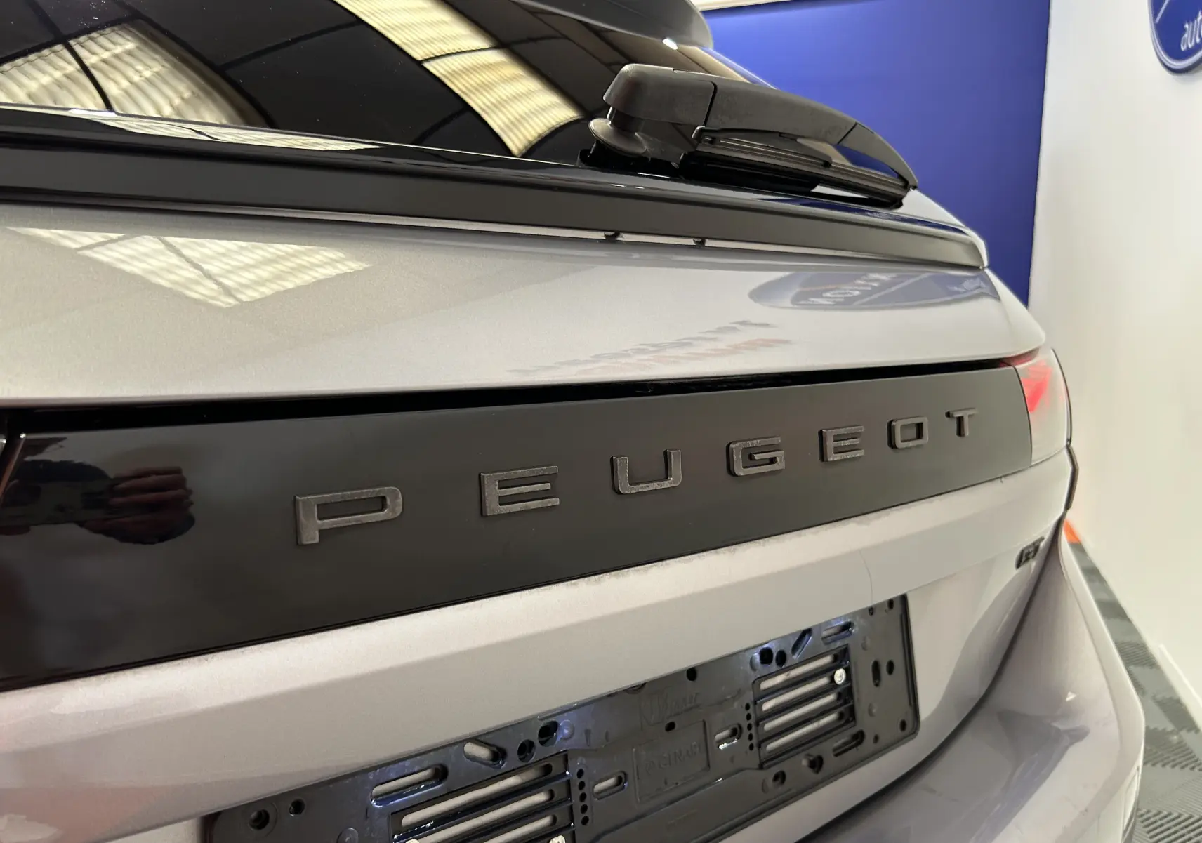 Gros plan sur l'arrière gris artense du Peugeot 508 SW 2024 avec logo Peugeot et hayon ouvert partiellement.