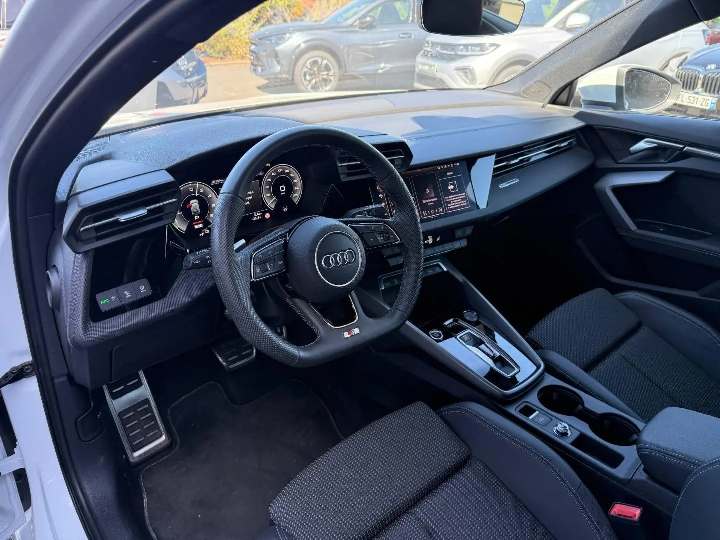 Vue intérieure côté conducteur de l'Audi A3 Sportback blanc Glacier, volant sport et tableau de bord numérique.