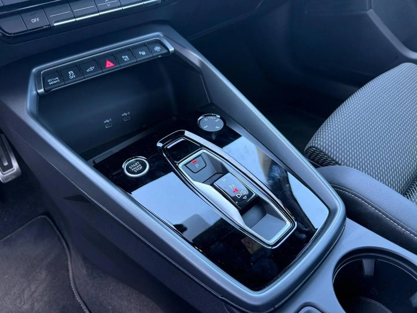 Gros plan sur la console centrale noire brillante de l’Audi A3 Sportback 2025 avec levier de vitesse automatique et bouton start/stop.