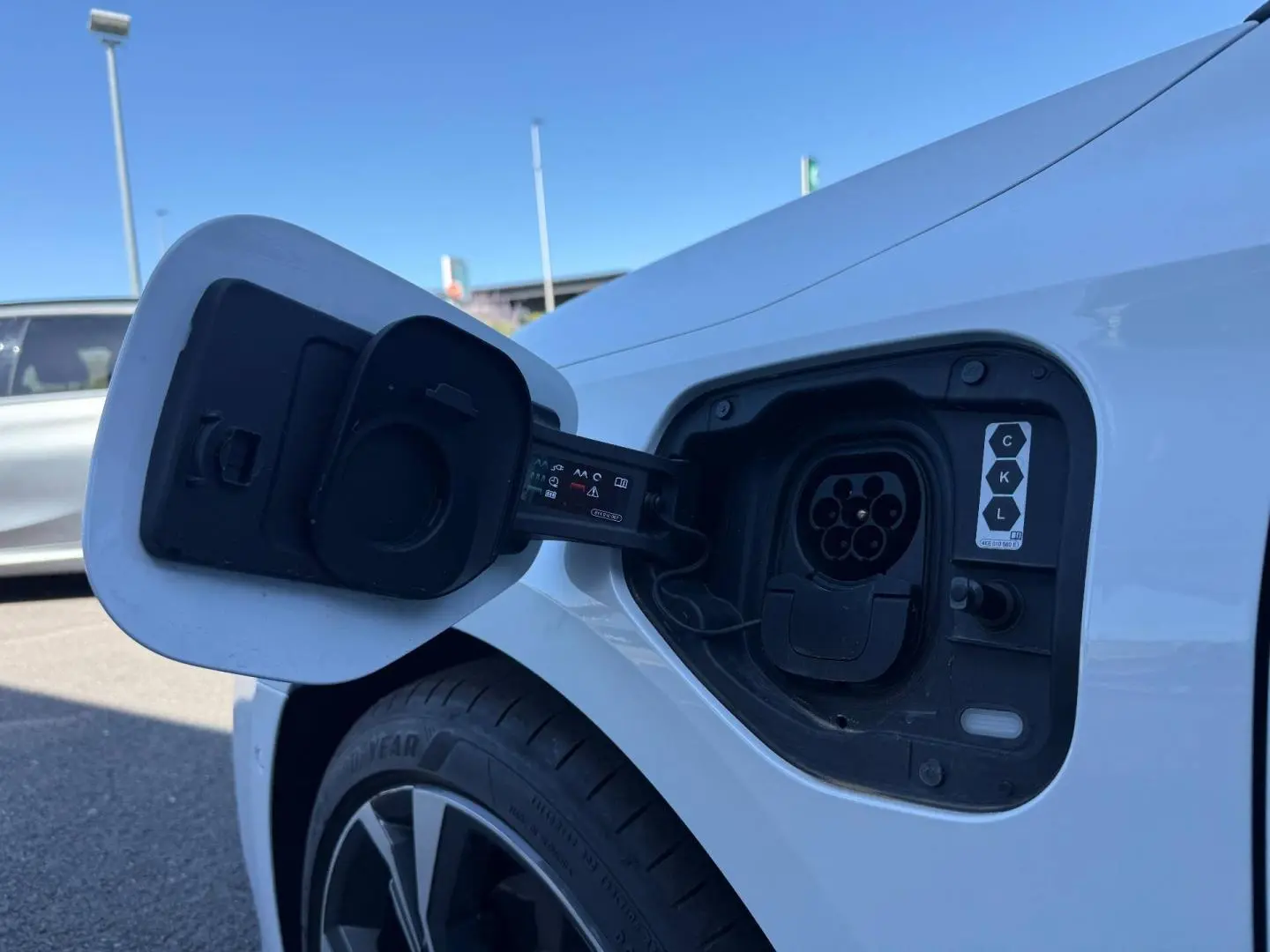 Prise de recharge ouverte côté arrière droit d’une Audi A3 Sportback blanche Glacier métallisé, jante alu visible.