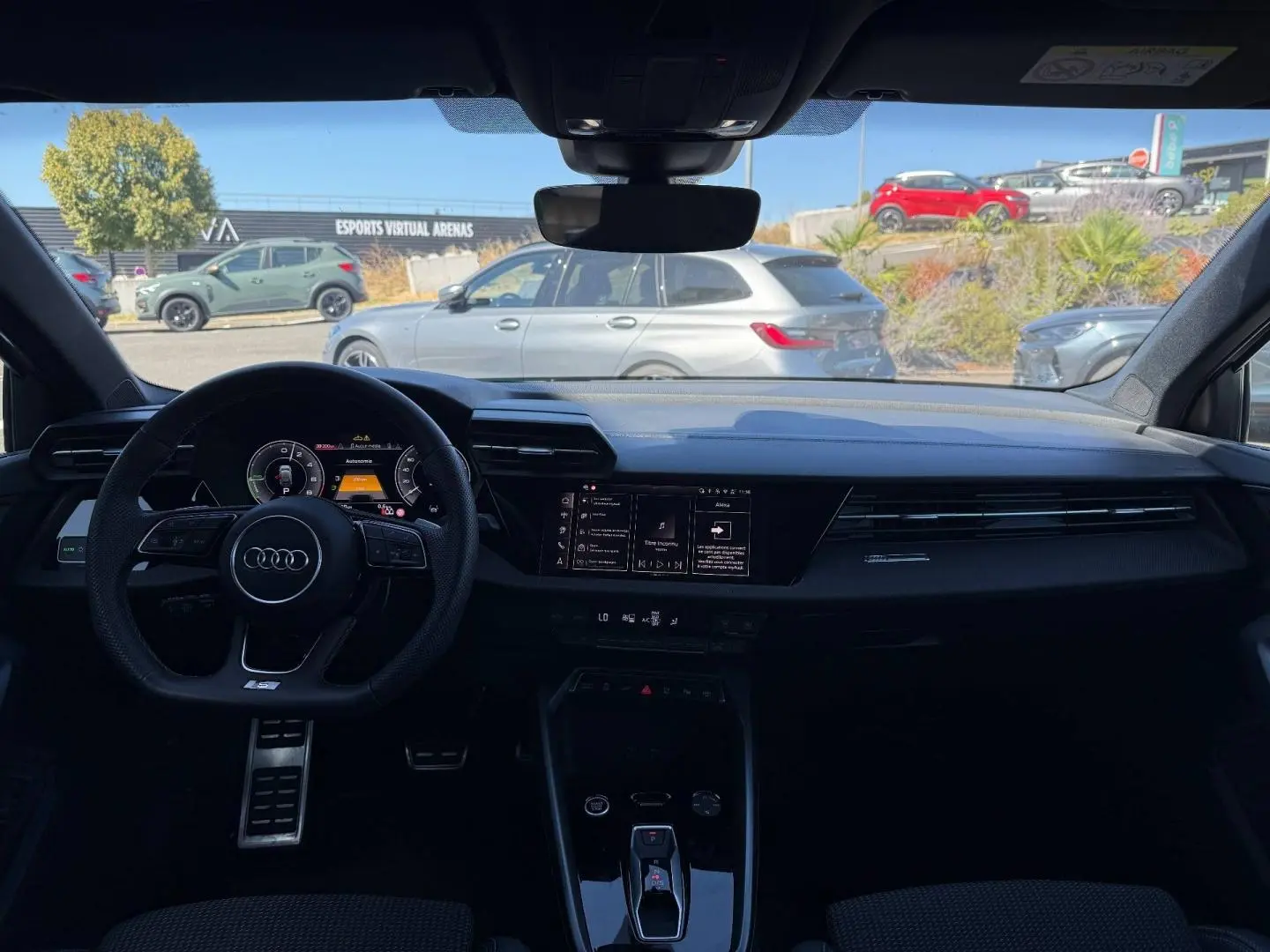 Vue intérieure avant de l'Audi A3 Sportback 2025 hybride, tableau de bord noir avec volant sport et écran tactile central.