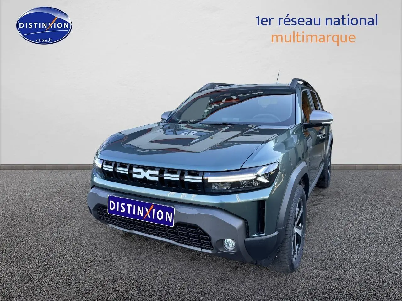 Dacia Duster 2025 vert cèdre en 3/4 avant droit, avec jantes alu et barres de toit visibles.
