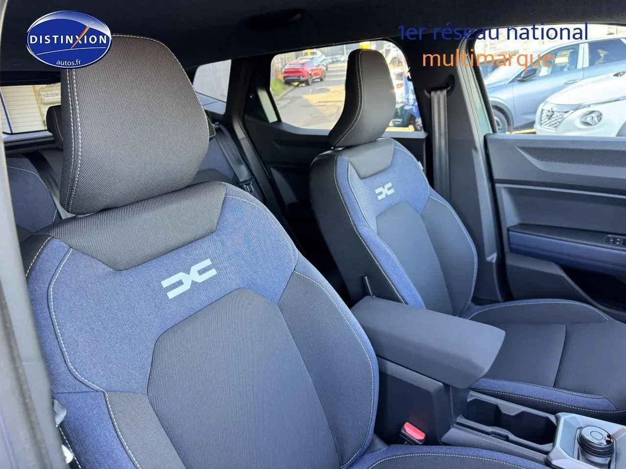 Vue intérieure rapprochée des sièges avant bleu et noir du Dacia Duster 2025 avec accoudoir central et logo distinctif brodé.