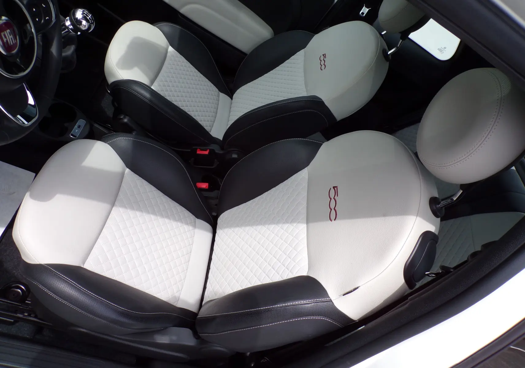 Vue plongeante sur les sièges avant bi-ton noir et blanc avec logo 500 brodé dans une Fiat 500 blanche de 2019.