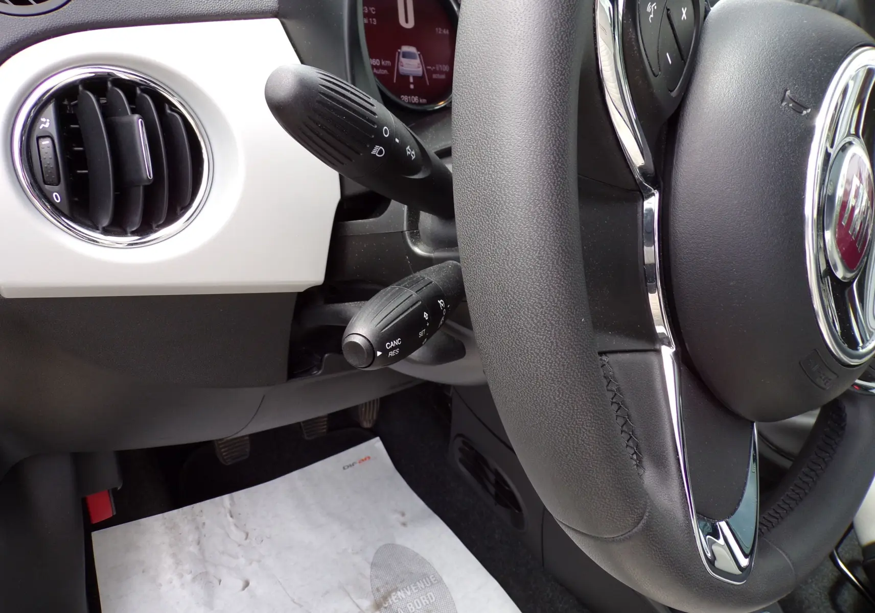 Gros plan sur le volant noir et la console blanche de la FIAT 500 2019, avec commandes au volant visibles.