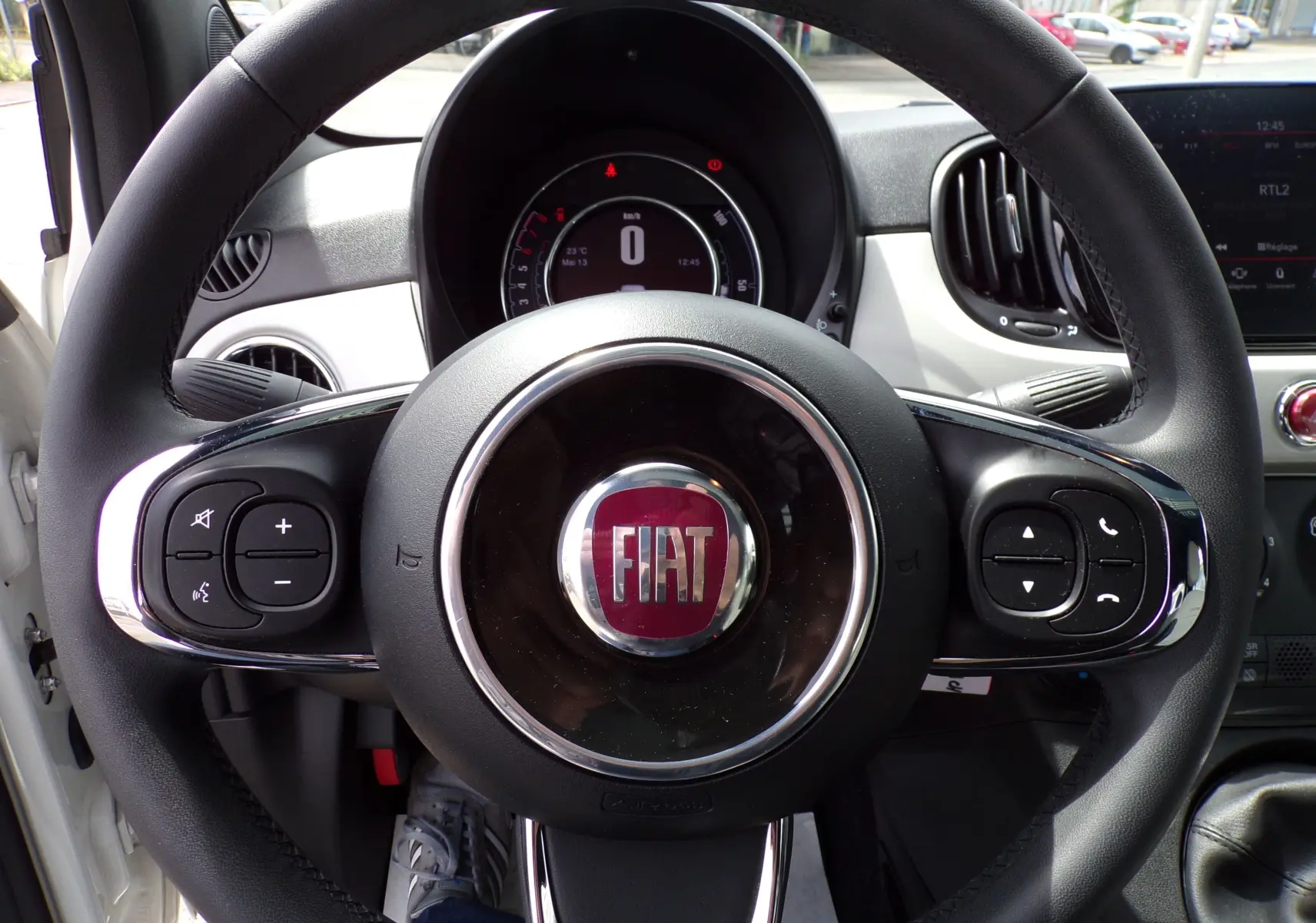 Vue rapprochée du volant noir de la Fiat 500 blanche de 2019 avec commandes intégrées et tableau de bord numérique.