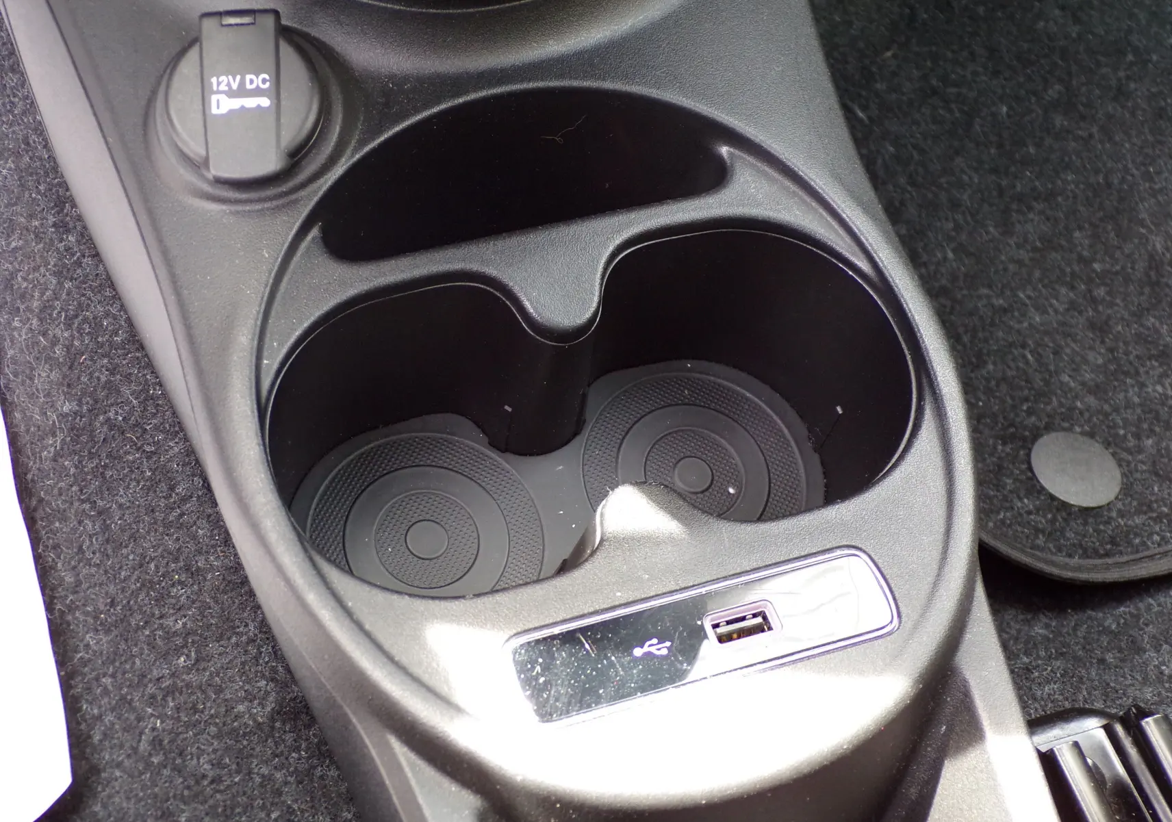 Prise USB et porte-gobelets noirs en gros plan dans la console centrale de la Fiat 500 blanche de 2019.