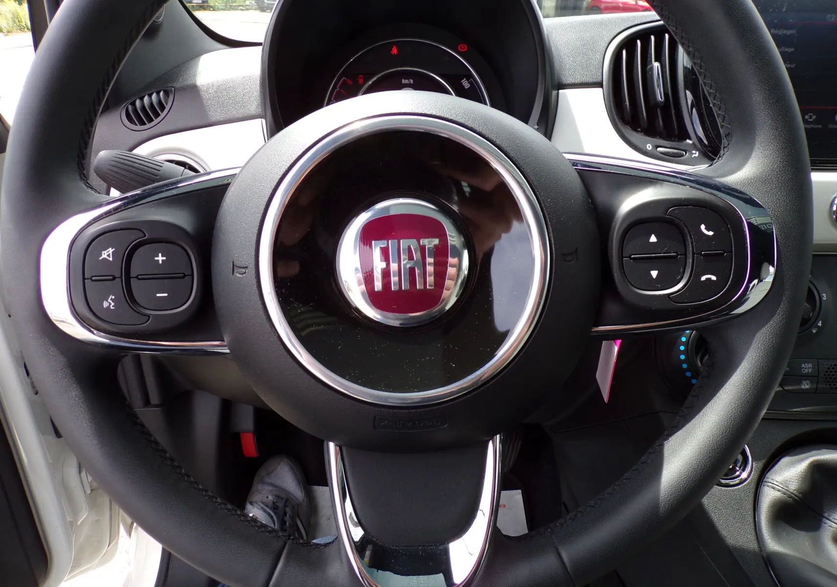 Volant noir de Fiat 500 blanc 2019 vu de face, avec commandes intégrées et logo Fiat central rouge.