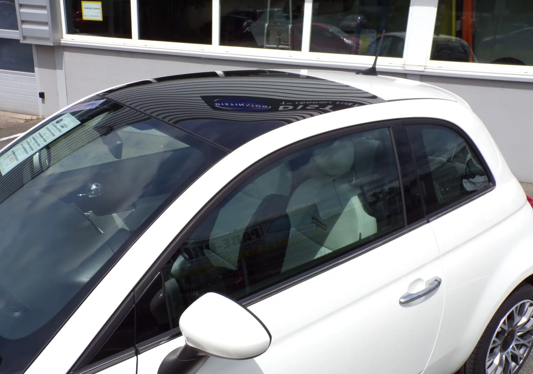 Vue côté droit en 3/4 avant d'une Fiat 500 blanche avec toit noir brillant et jantes alliage 16 pouces bicolores.