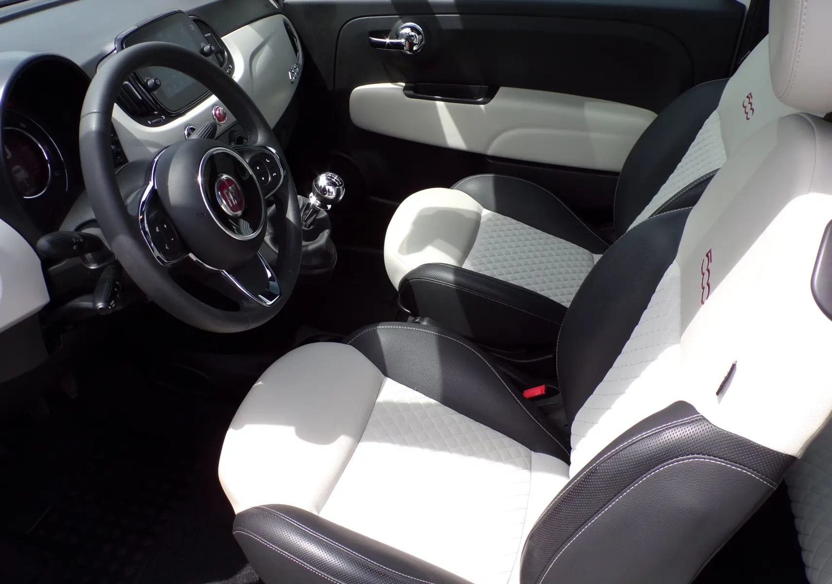 Intérieur de la Fiat 500 blanc et noir vu côté conducteur, avec volant multifonction et sellerie bi-ton élégante.