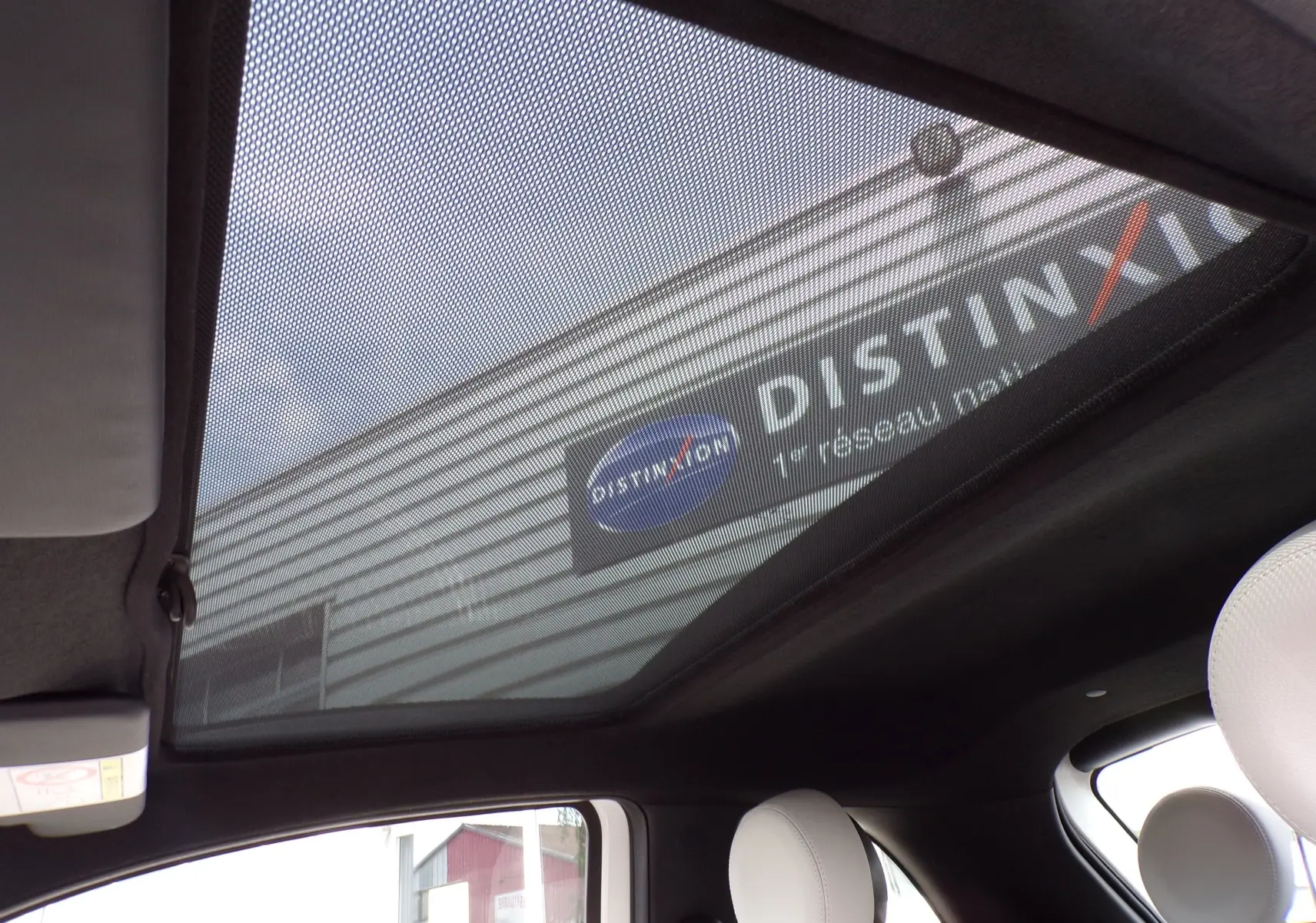 Toit panoramique en verre avec pare-soleil sur l'intérieur d'une Fiat 500 blanche, vue de l'habitacle vers le haut.