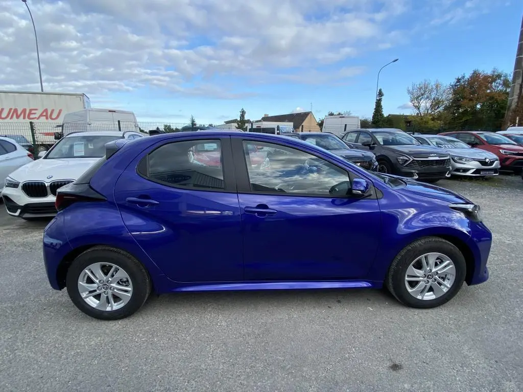 Profil côté gauche d'une Toyota Yaris 2025 hybride bleu Genièvre avec jantes alliage 15 pouces sur parking.