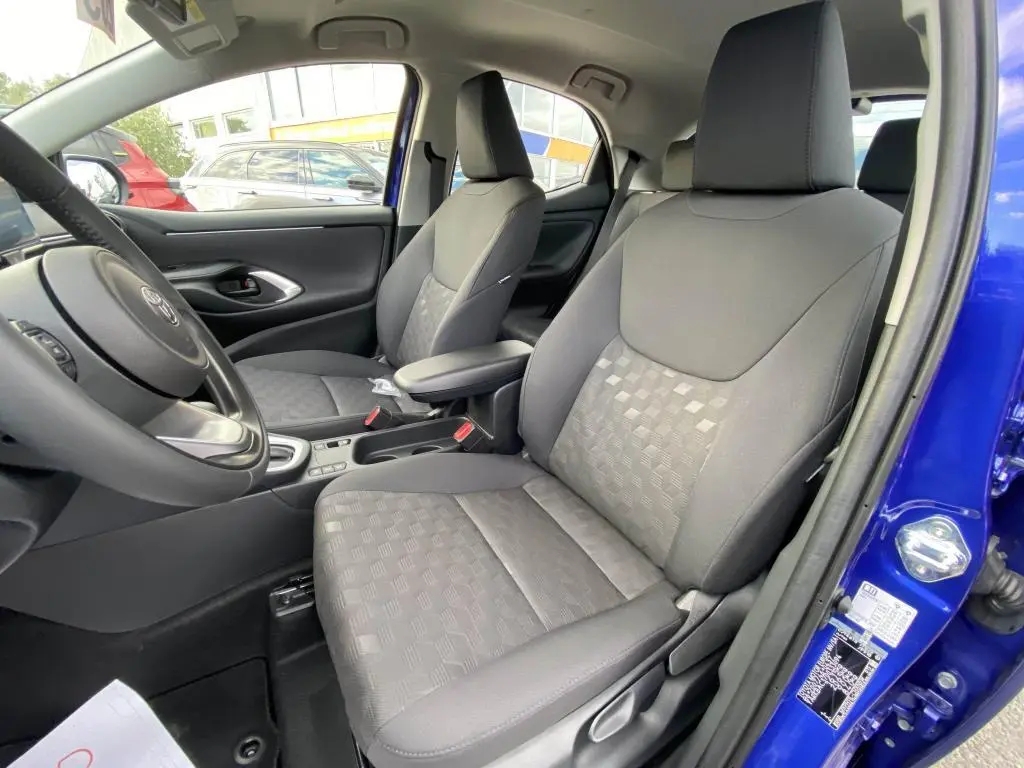 Vue intérieure côté conducteur de la Toyota Yaris 2025 bleu Genièvre, montrant les sièges avant en tissu gris et la porte ouverte.