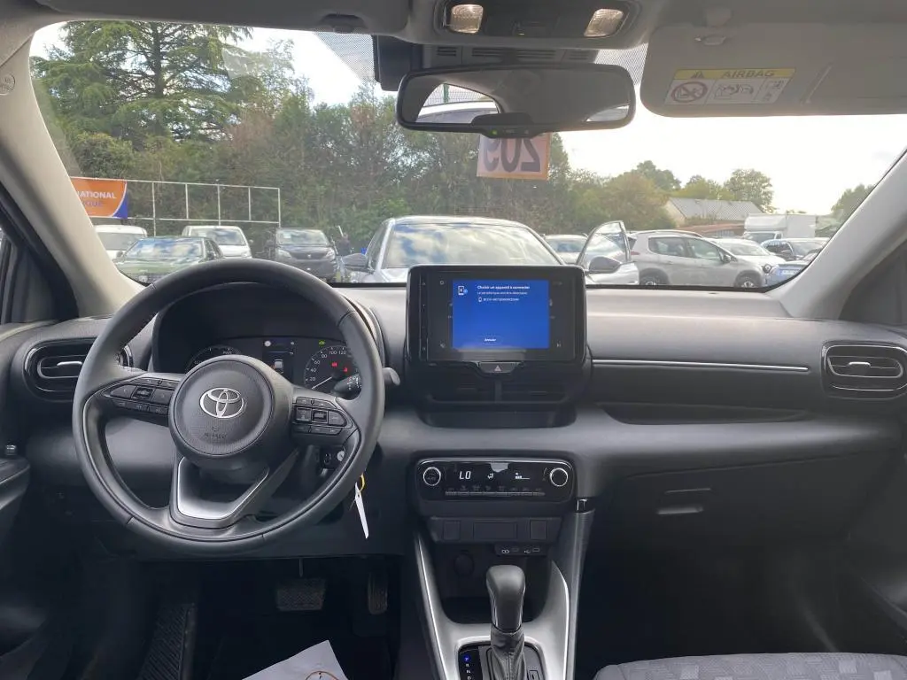Vue intérieure frontale du tableau de bord et volant de la Toyota Yaris hybride 2025, avec écran tactile central allumé.