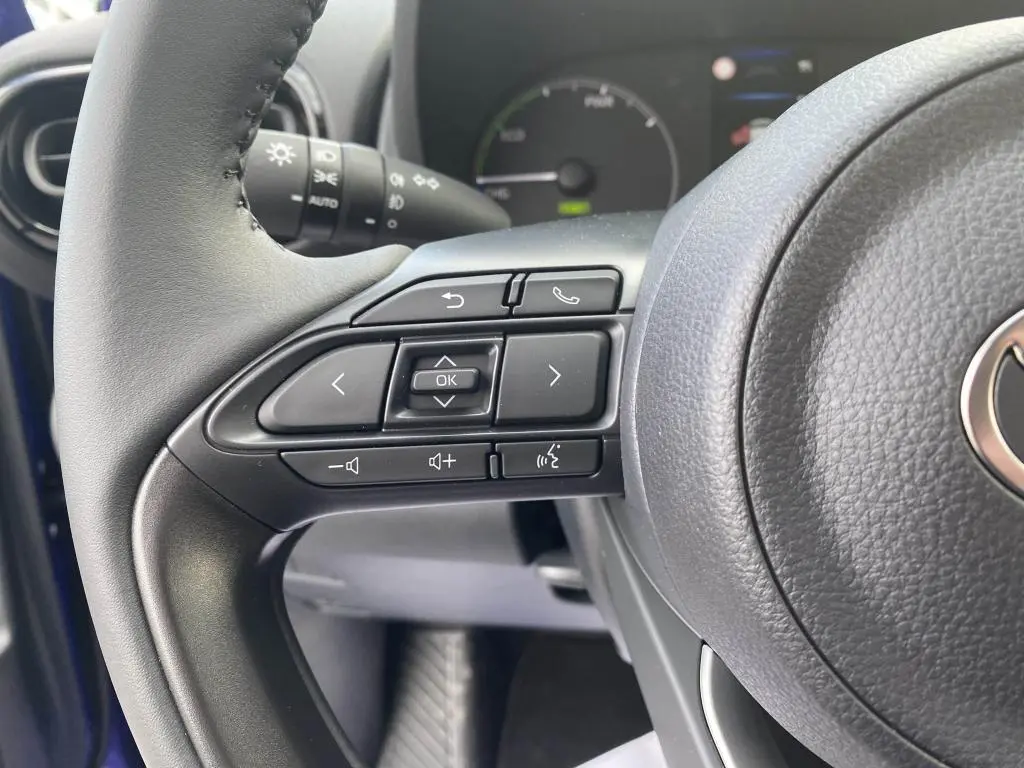 Gros plan sur les commandes au volant côté gauche de la Toyota Yaris hybride 2025, intérieur noir.