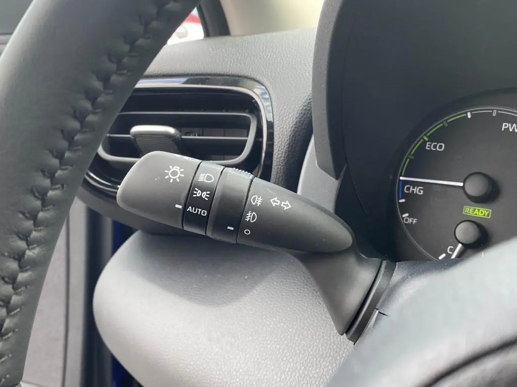 Gros plan sur la commande d'éclairage à gauche du volant dans l'habitacle d'une Toyota Yaris hybride 2025 Bleu Genièvre.