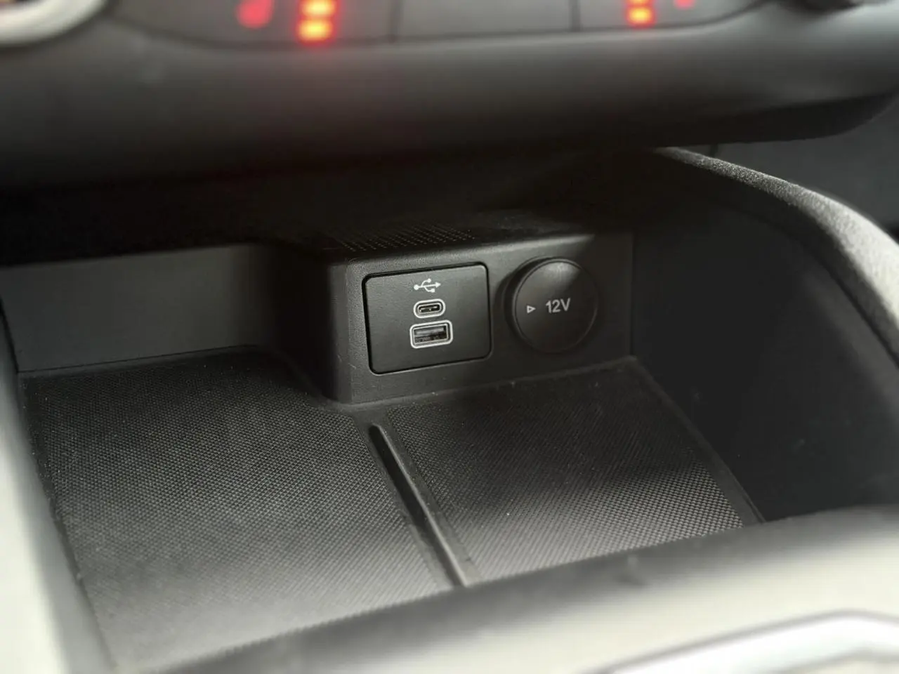 Gros plan sur la console centrale du Ford Kuga 2024 montrant les ports USB et la prise 12V dans un intérieur noir.