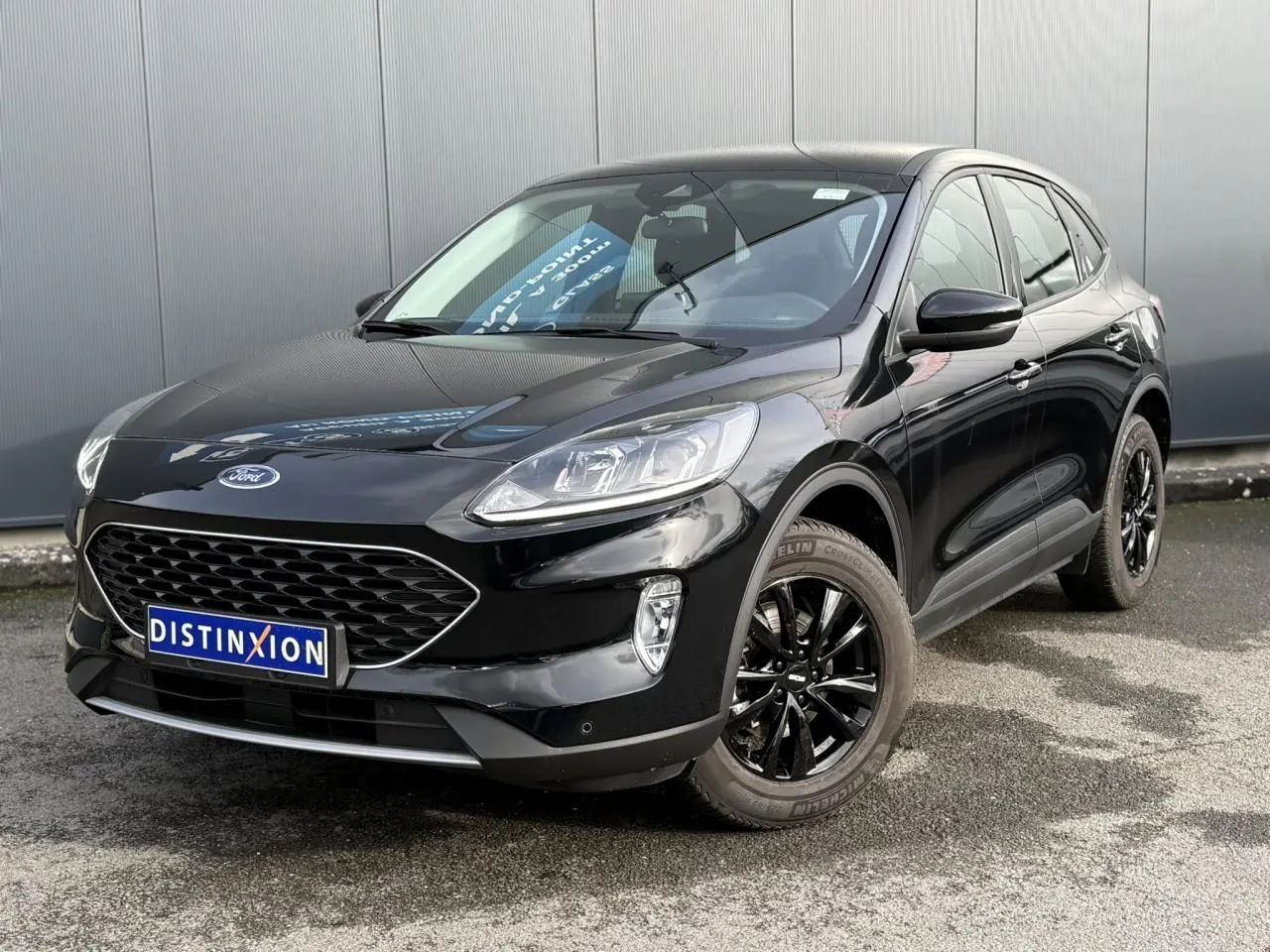 Ford Kuga 2024 noir obsidien en 3/4 avant droit avec jantes alliage noires et attelage rétractable visible.