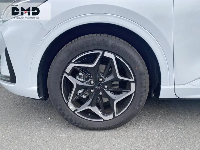 Gros plan sur la roue avant droite avec jante alu 19 pouces noir et argent du Ford Kuga blanc Glacier.