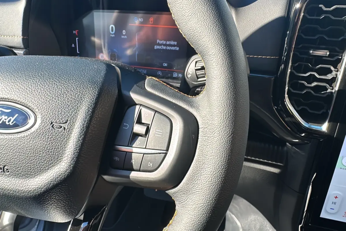 Vue rapprochée du volant cuir multifonctions noir du Ford Ranger Wildtrak Plus 2026 avec écran digital en arrière-plan.