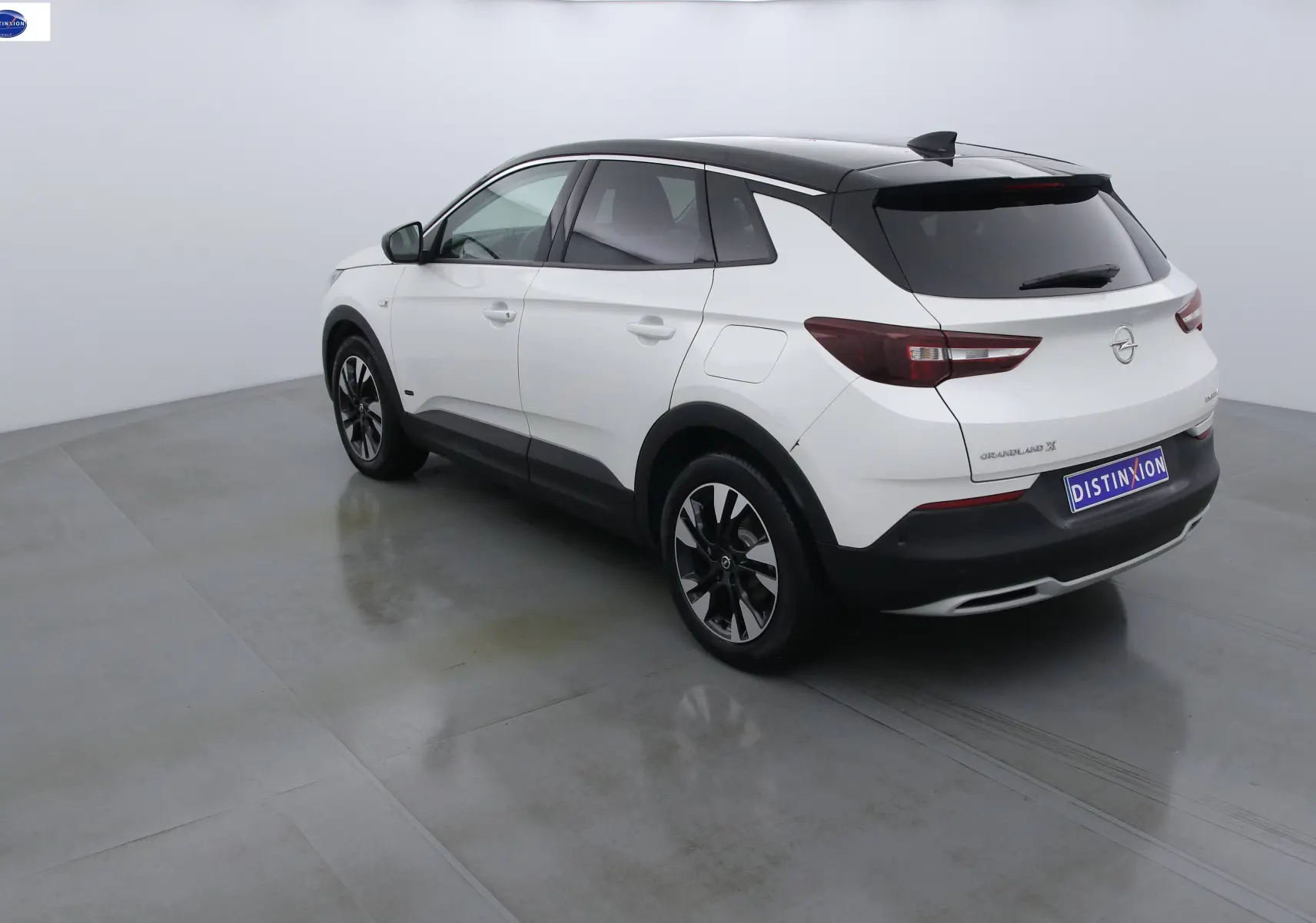 Opel Grandland X hybride blanc perle métal vu en 3/4 arrière côté gauche avec toit noir et jantes bicolores.