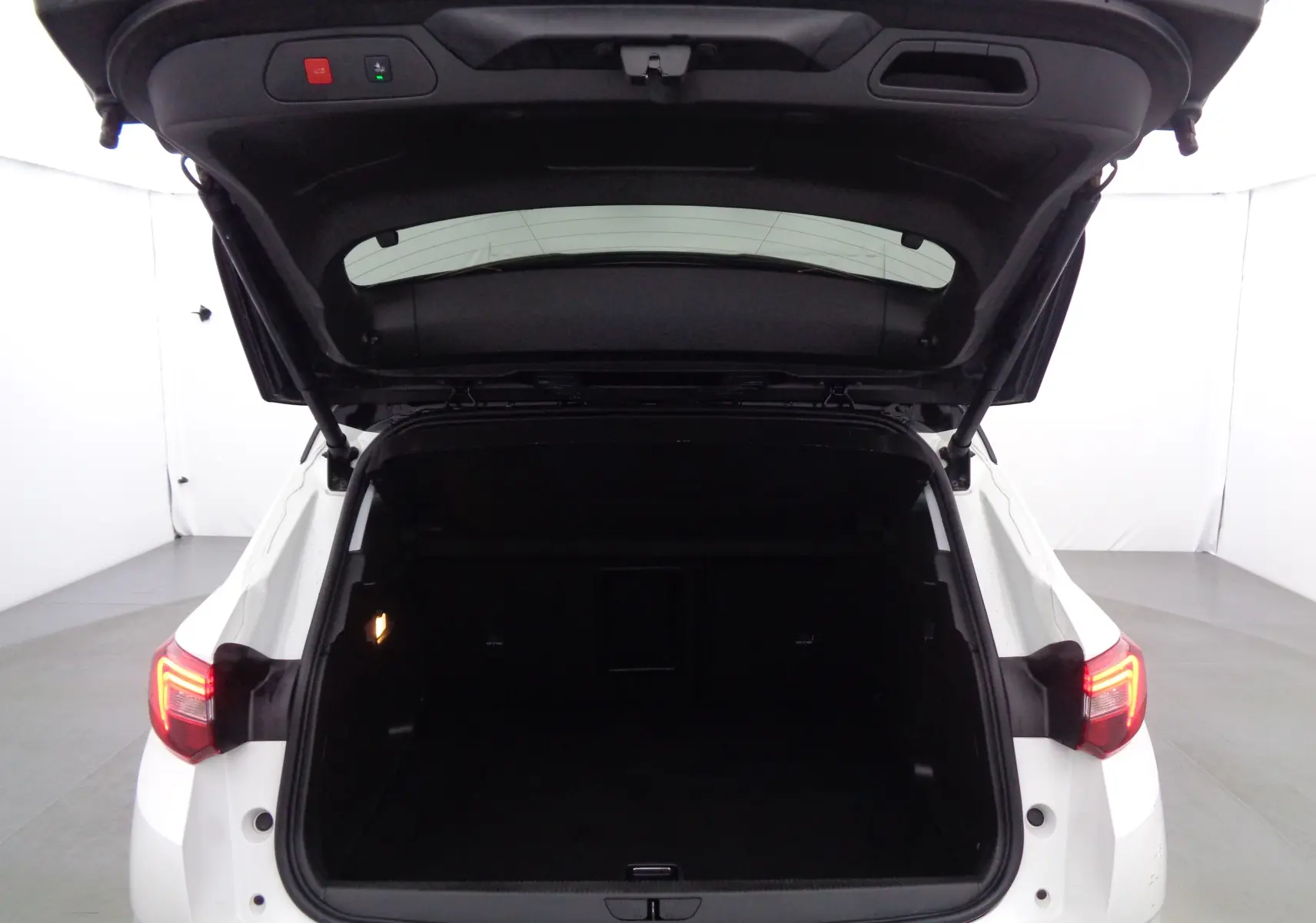 Coffre ouvert vu de l'arrière d'un Opel Grandland X blanc perle métal, avec feux arrière allumés dans un studio.