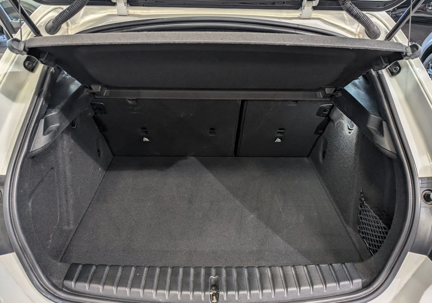 Coffre ouvert vu de l'arrière d'une BMW Série 1 F40 blanche, montrant un espace de chargement propre et spacieux.