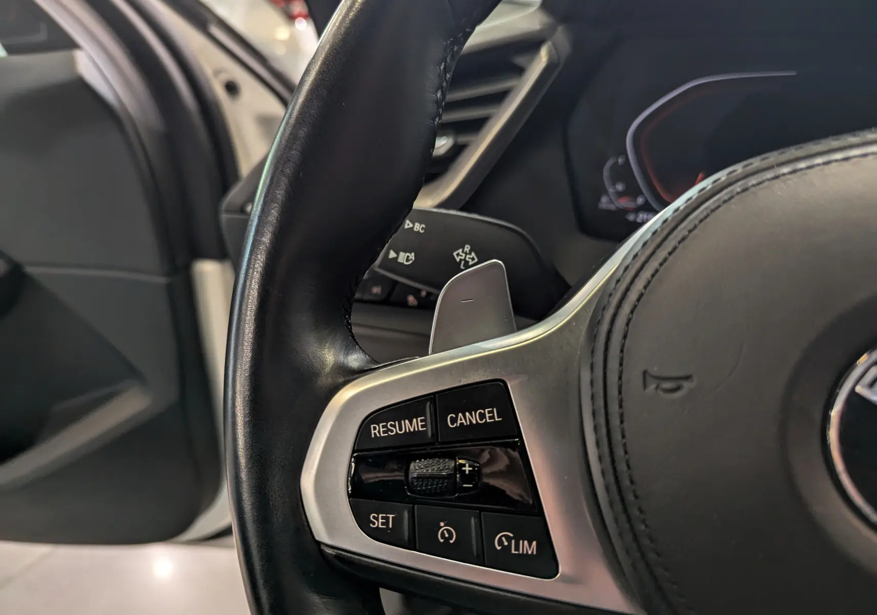 Gros plan sur les commandes de régulateur de vitesse au volant cuir noir d'une BMW Série 1 F40 blanche.