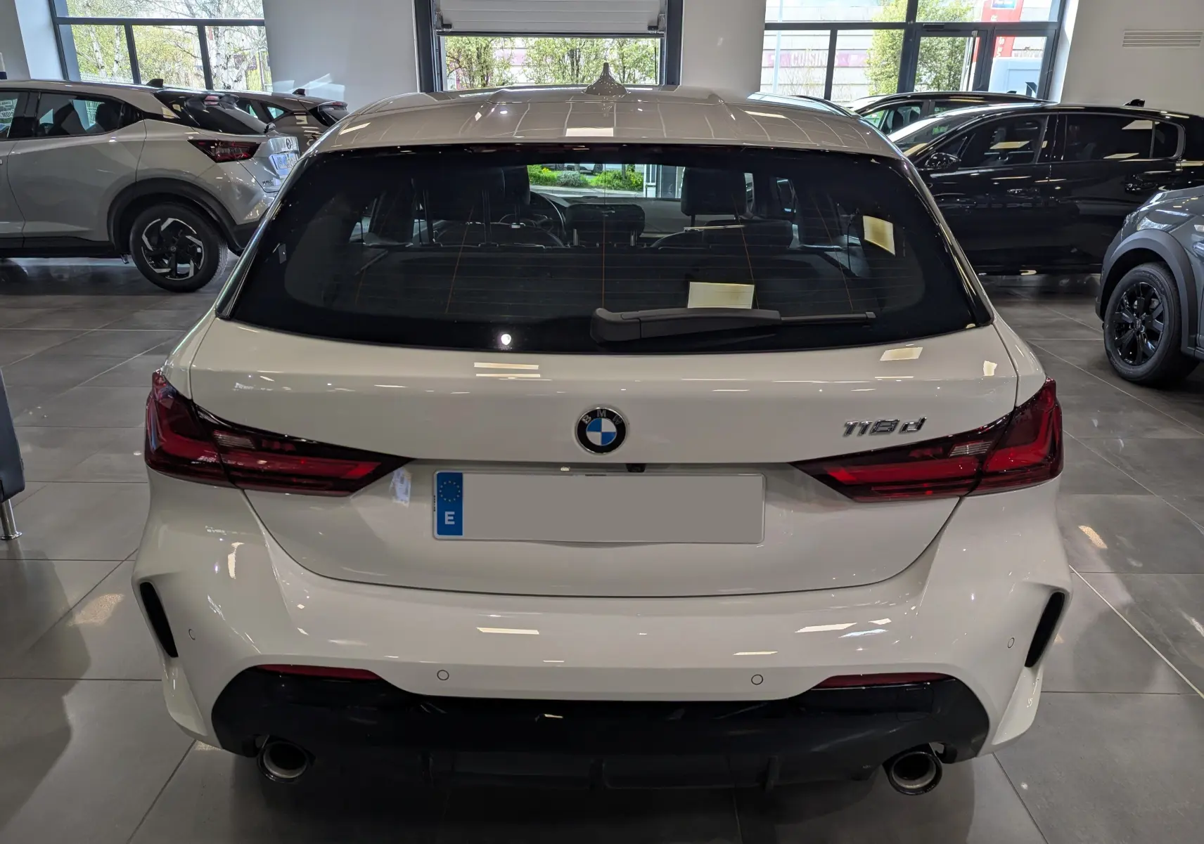 Vue arrière d'une BMW Série 1 F40 18d blanche Alpine avec feux LED et double sortie d'échappement en concession.