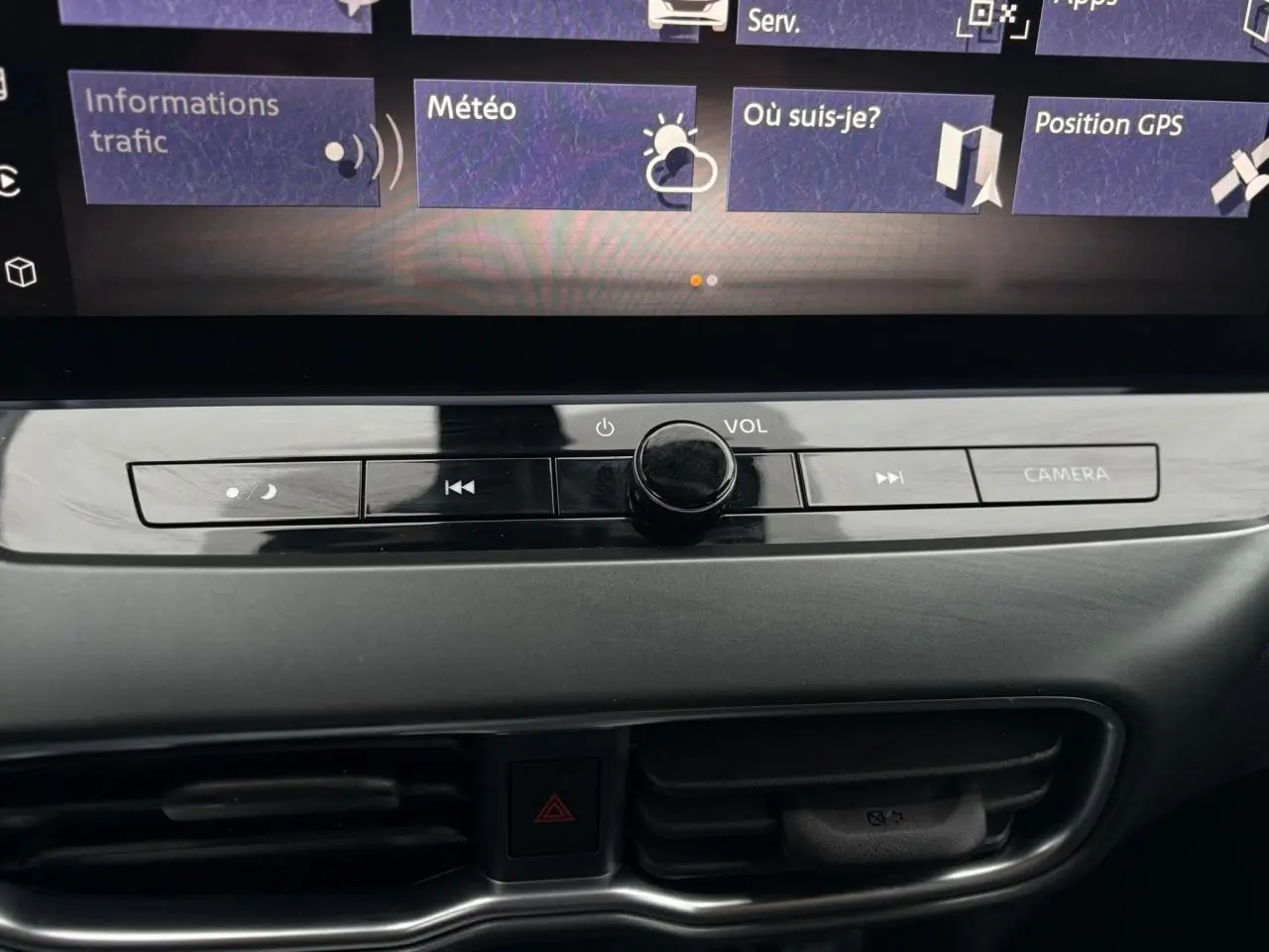 Gros plan sur la console centrale du Nissan Juke blanc nacré 2025, avec commandes volume et bouton caméra visibles.