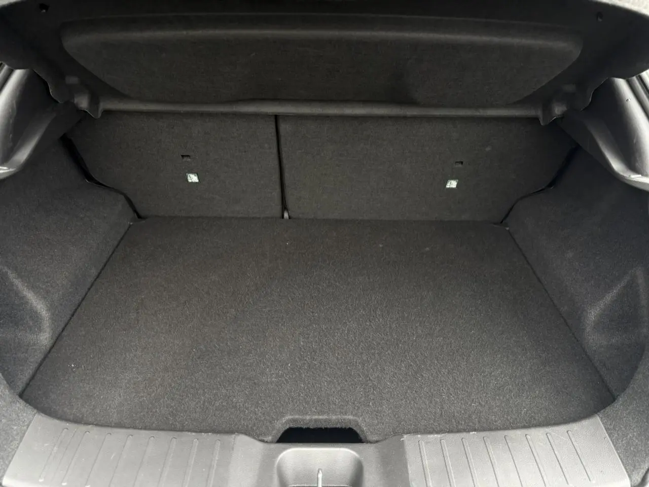 Coffre ouvert du Nissan Juke blanc nacré 2025, montrant un espace de chargement propre et tapissé de tissu gris.