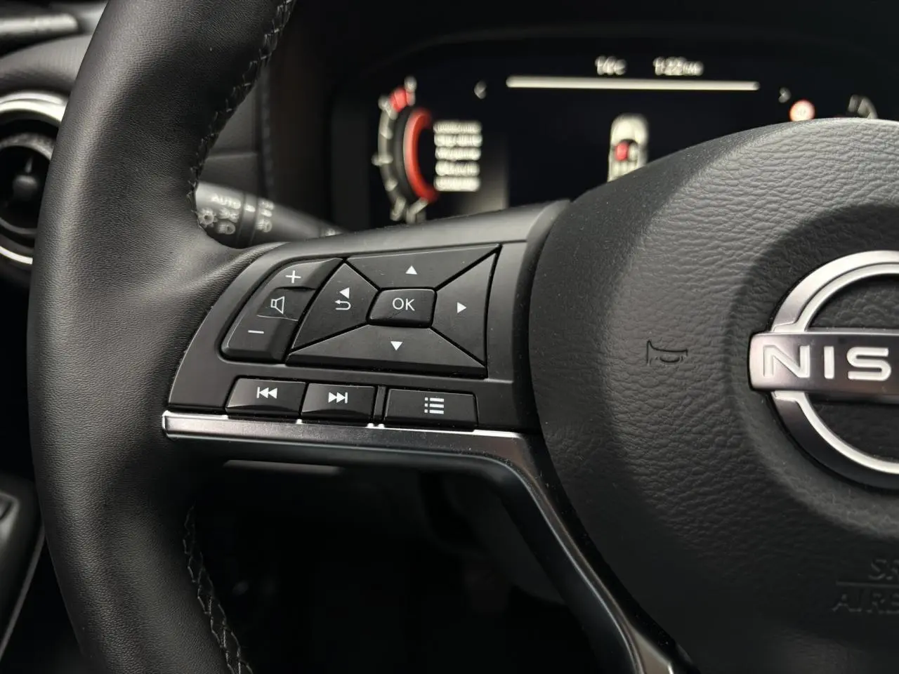 Gros plan sur le volant en cuir noir côté gauche du Nissan Juke 2025 avec commandes multifonctions et tableau de bord digital flou.