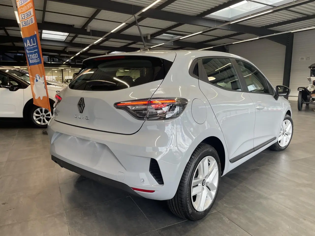 Vue 3/4 arrière droite d'une Renault Clio 2025 gris Rafale avec feux arrière LED et jantes alliage en showroom.
