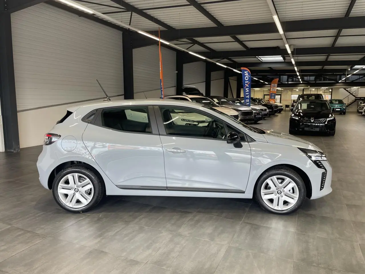 Profil côté gauche d'une Renault Clio 2025 gris Rafale avec jantes alliage et poignées couleur carrosserie en showroom.