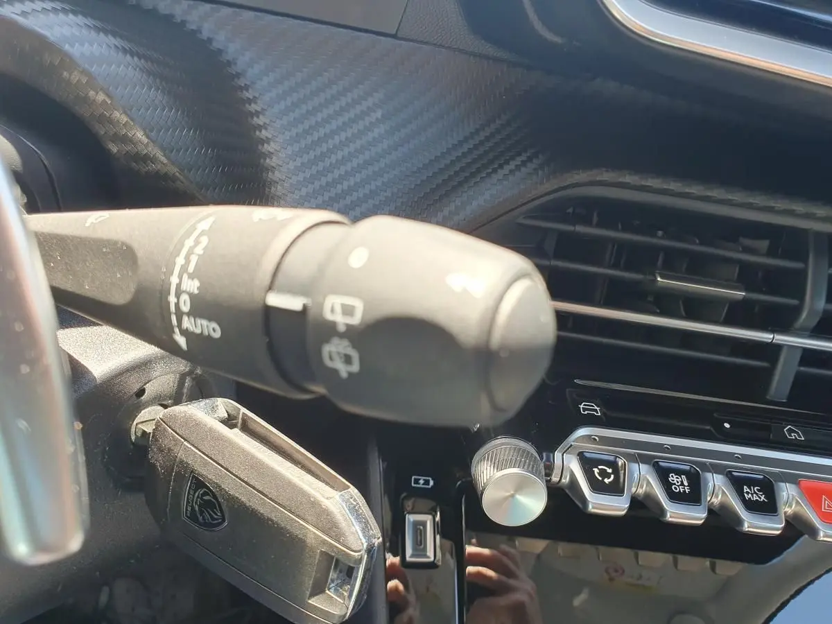 Détail intérieur du tableau de bord de la Peugeot 208 gris Artense, avec commandes d’essuie-glace et boutons de climatisation.