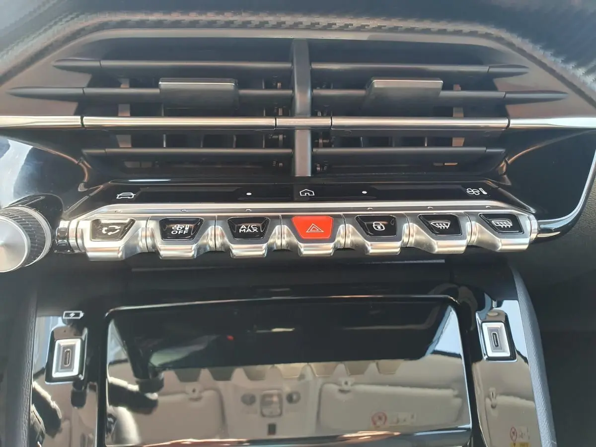 Vue rapprochée de la console centrale de la Peugeot 208 1.2 Hybrid 110, boutons argentés et noir brillant.