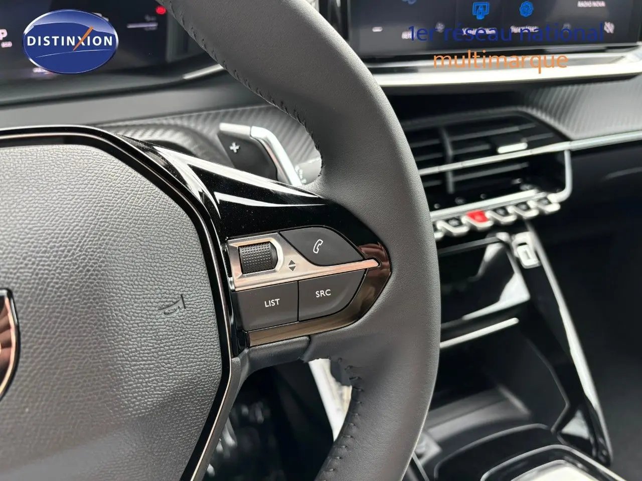Gros plan sur le volant en cuir noir et les commandes multimédia du Peugeot 2008 Hybrid 136ch Allure, intérieur moderne.