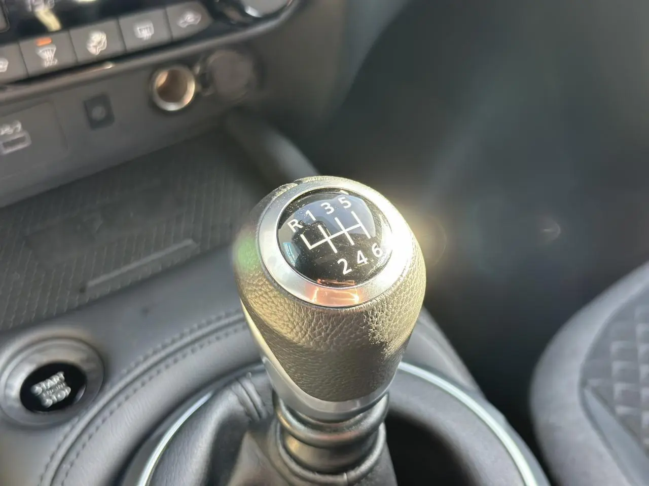 Gros plan sur le levier de vitesses manuel noir du Nissan Juke 2025, avec console et siège partiellement visibles.