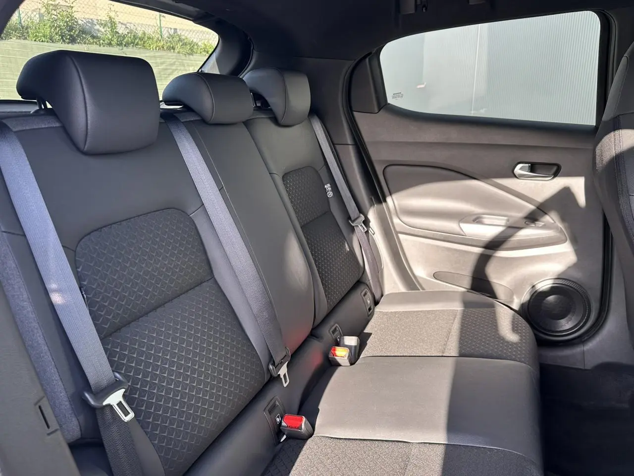 Vue latérale droite de la banquette arrière noire du Nissan Juke 2025 avec ceintures de sécurité et haut-parleur intégré.