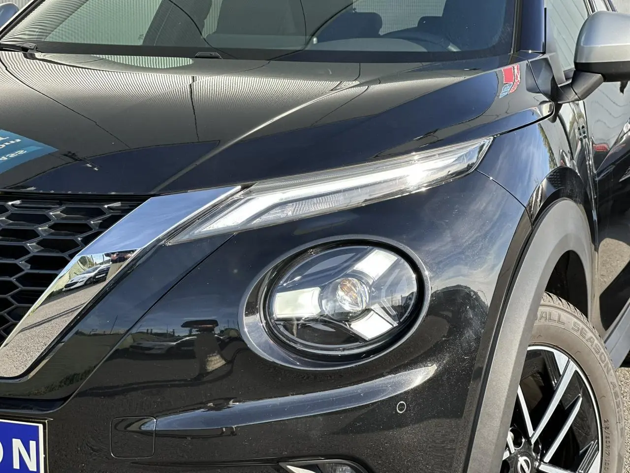 Gros plan sur l'avant droit noir du Nissan Juke 2025, mettant en valeur le phare rond et la calandre chromée.