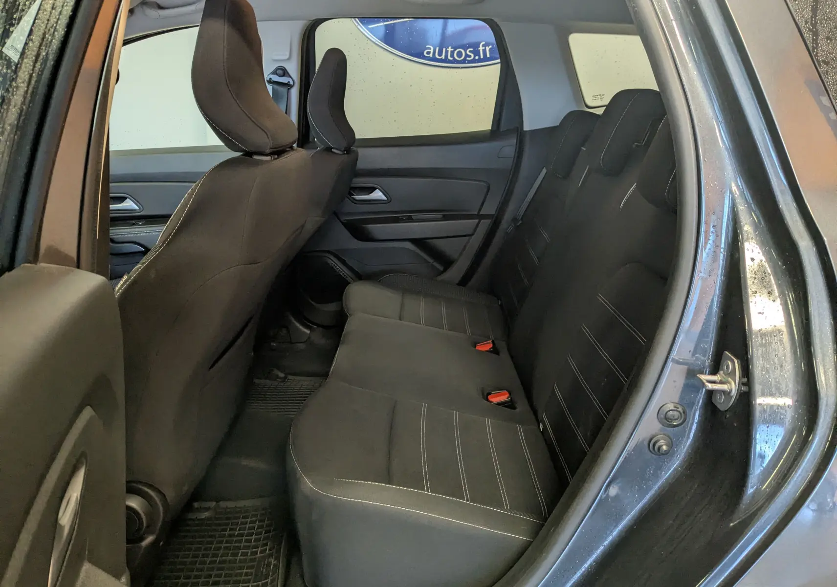 Vue intérieure arrière côté droit du Dacia Duster gris 2023, montrant les sièges en tissu noir avec surpiqûres blanches.