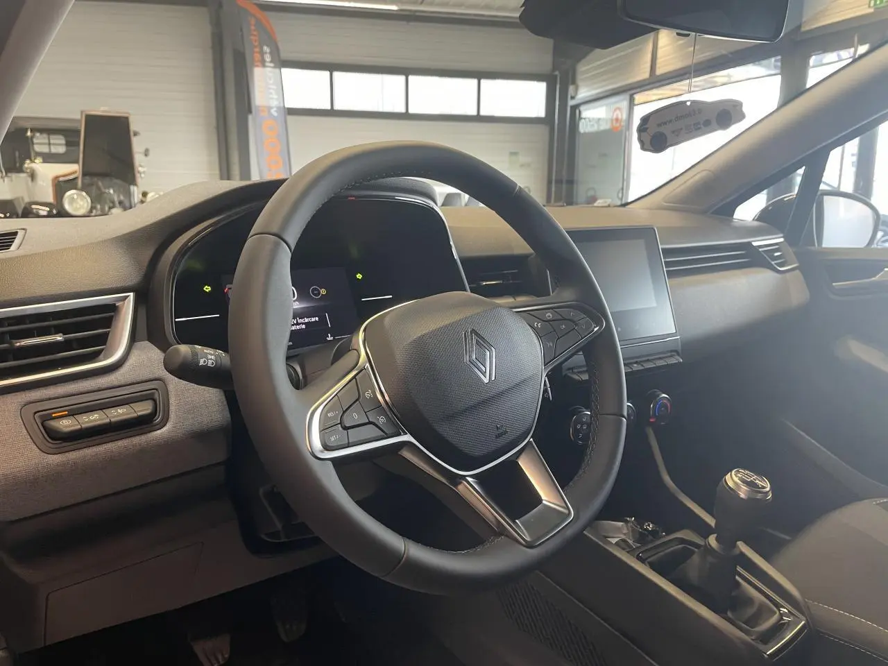 Vue intérieure centrée sur le volant multifonction et la console centrale d'une Renault Clio 2025 noire étoile.